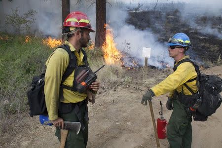 Firefighters Will Smith (L) and Ben Delyea (R) converse as they keep watch over a controlled burn while battling the Carlton Complex Fire near Winthrop, Washington July 19, 2014. REUTERS/David Ryder