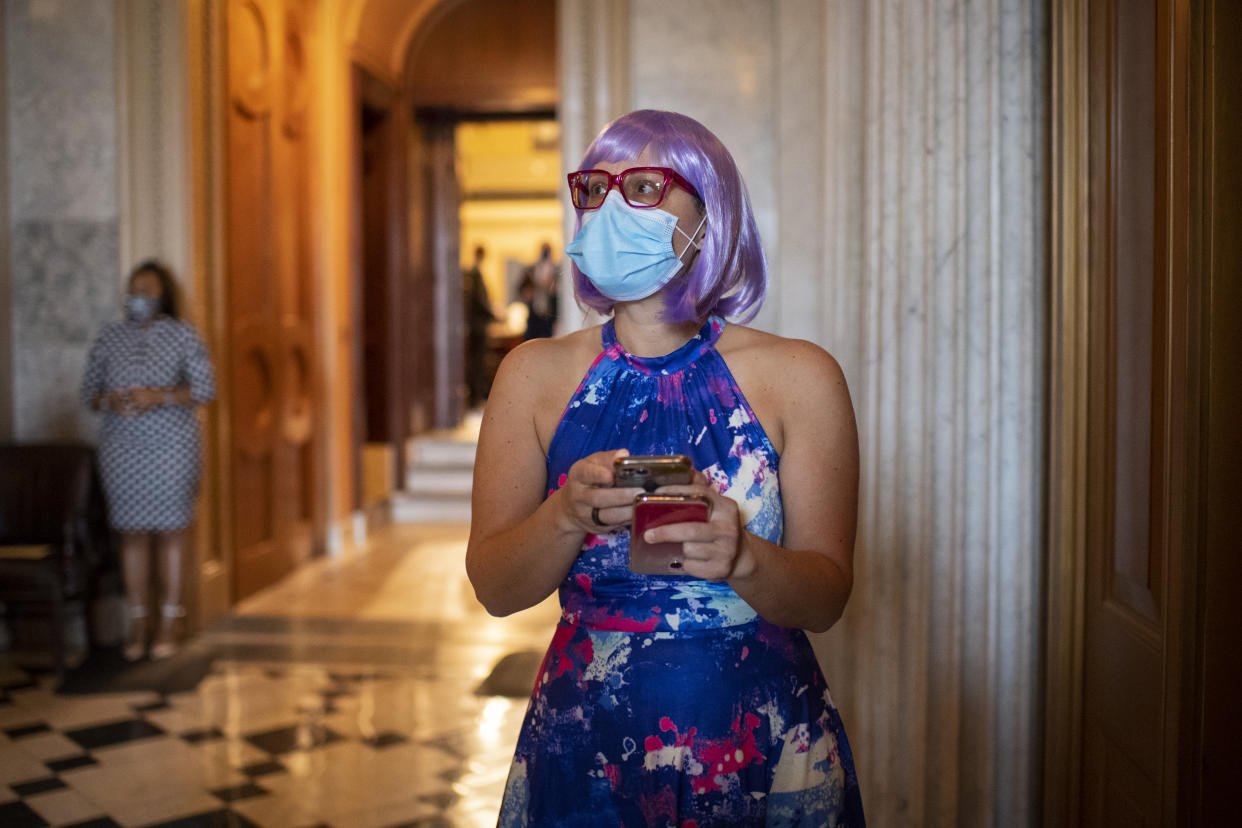 Sen. Kyrsten Sinema holds two phones while wearing a face mask and purple wig.