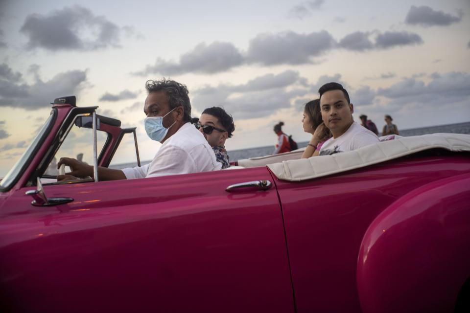 FILE - In this March 13, 2020 file photo, a taxi driver wears a protective mask as he drives tourists in his classic American car in Havana, Cuba. Across Latin America, coronavirus is taking root in the world's most unequal region. (AP Photo/Ramon Espinosa, File)