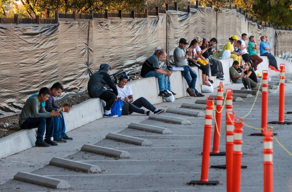 Migrantes venezolanos se sientan y atienden sus teléfonos móviles en el estacionamiento cerrado del Centro de Recursos para Migrantes de San Antonio.