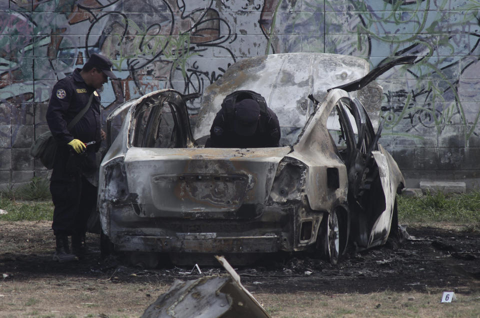 Police review the charred remains of a car that exploded as authorities responded to a report of a vehicle with a corpse inside, in the San Bartolo neighborhood of Soyapango, El Salvador, Monday, April 29, 2019. Two police officers were injured in the explosion. (AP Photo/Salvador Melendez)