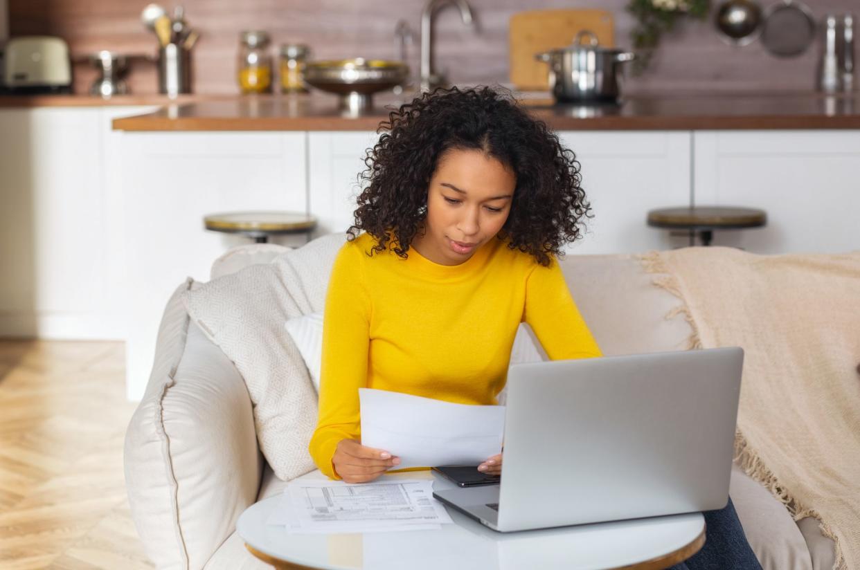 Young African American woman analyzing budget or utility bills sitting on the couch at home