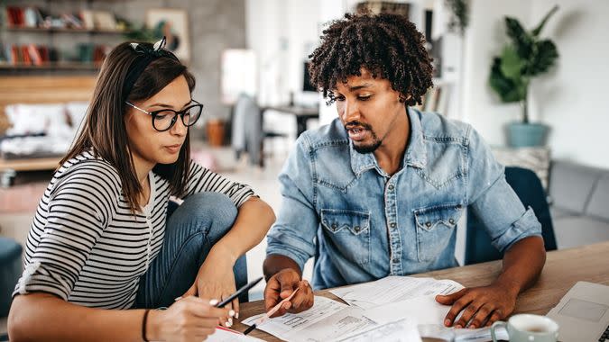 Modern married multi-ethnic young couple calculating financial bills at home.