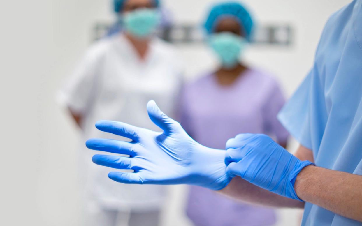 Surgeon putting on latex glove - Science Photo Library