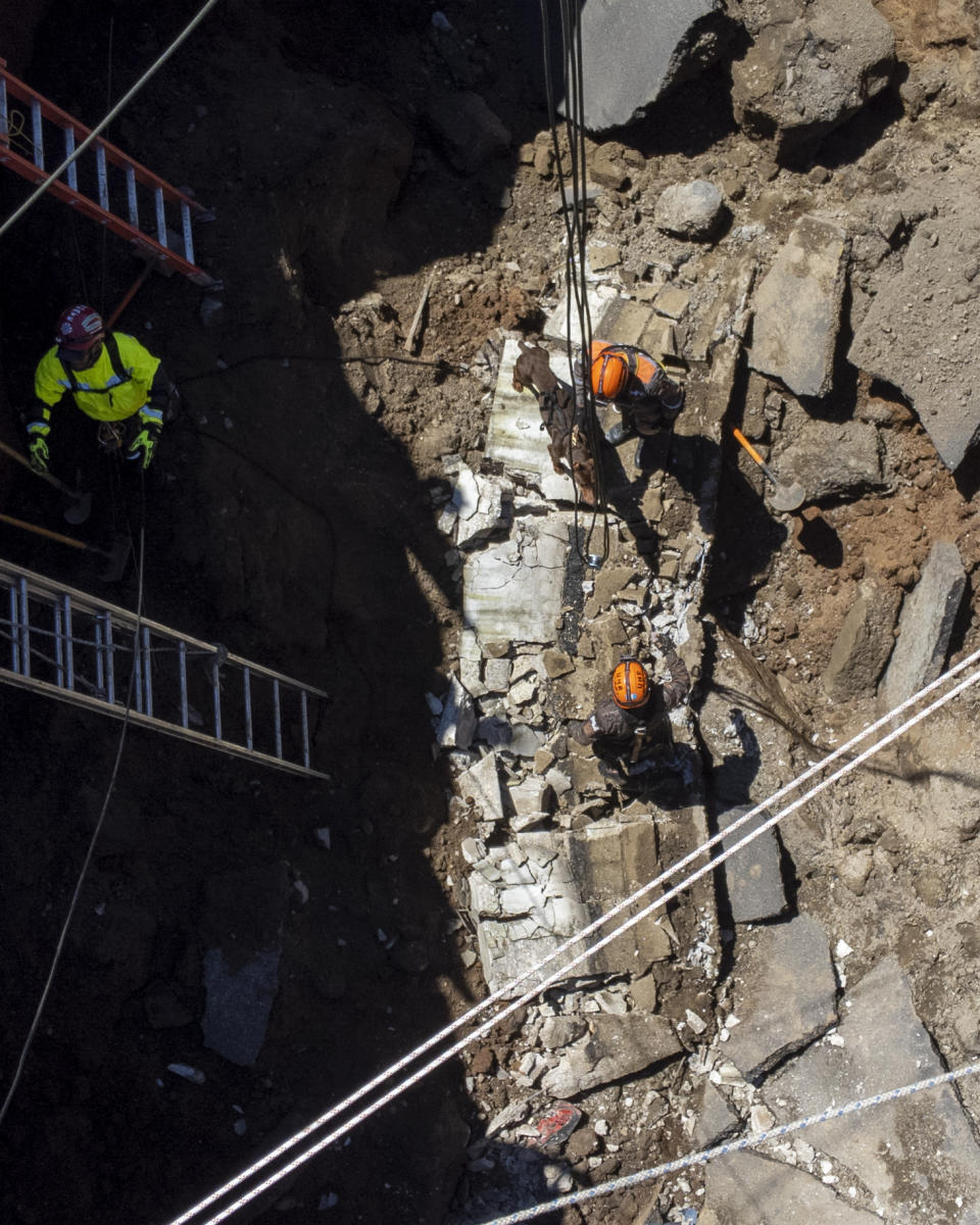 Rescuers search for victims inside a sinkhole in Villa Nueva, Guatemala, Sunday, Sept. 25, 2022. Rescuers are searching for people who are believed to have fallen into the sinkhole while driving their vehicle, while four others were rescued alive from the scene on Saturday night. (AP Photo/Moises Castillo)