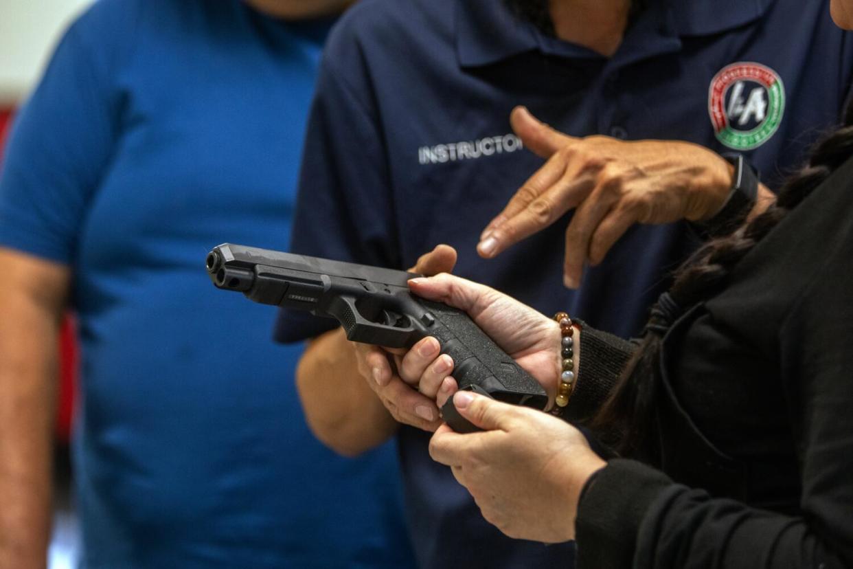 A close-up of Nikki Shrieve's hands holding a Glock pistol as instructor Tom Nguyen gestures to it