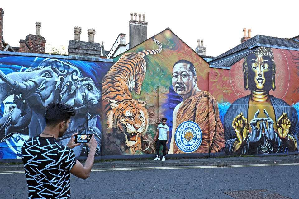 <p>A man takes a picture of his friend standing next to a mural of the Leicester City owner Vichai Srivaddhanaprabha. Aaron Chown/PA Wire </p>