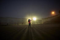 FILE- A woman records with her phone, as floodlights from the United States light up the newly-fortified border wall Thursday, Jan. 10, 2019, along the beach in Tijuana, Mexico. Top Trump administration officials will visit South Texas five days before Election Day to announce they have completed 400 miles of U.S.-Mexico border wall, attempting to show progress on perhaps the president's best-known campaign promise four years ago. But most of the wall went up in areas that already had smaller barriers. (AP Photo/Gregory Bull)