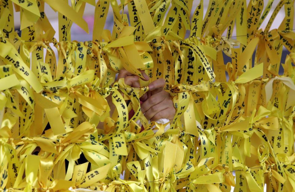 A woman ties yellow ribbons with messages for missing passengers aboard the sunken ferry boat Sewol in the water off the southern coast, in Seoul, South Korea, Friday, May 2, 2014. More than 300 people are dead or missing in the disaster that has caused widespread grief, anger and shame. (AP Photo/Lee Jin-man)