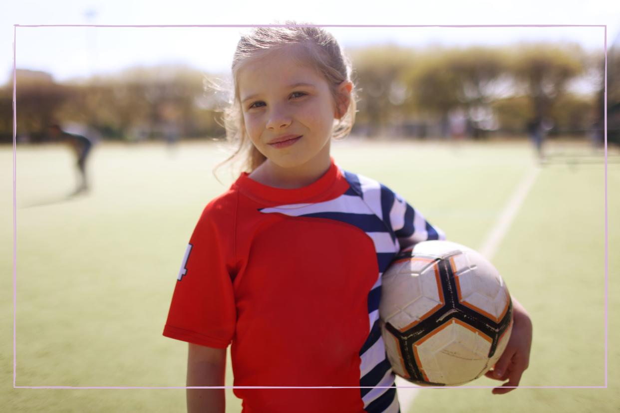  A young girl posing with a football under his arm. 