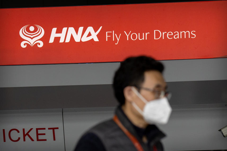 A man wearing a face mask to protect against the spread of the coronavirus walks past a ticket counter for Hainan Airlines, owned by Chinese firm HNA Group, at Beijing Capital International Airport in Beijing, Friday, March 6, 2020. HNA Group, a debt-burdened Chinese airline operator that faced opposition in Washington to its attempt to buy a Wall Street hedge fund during a costly global acquisition spree, says its creditors have asked a court to declare the company bankrupt. (AP Photo/Mark Schiefelbein)