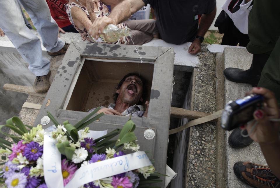 In this Feb. 5, 2014 photo, Divaldo Aguiar, who plays the part of Pachencho, lies inside a mock coffin as villagers splash rum into Aguiar's mouth during the Burial of Pachencho celebration at a cemetery in Santiago de Las Vegas, Cuba. The bash kicked off Wednesday with the slow procession to the local cemetery. Pallbearers carried the coffin of "Pachencho," who's known the other 364 days of the year as Divaldo Aguiar, to an open grave and used ropes to lower it six feet under. (AP Photo/Franklin Reyes)