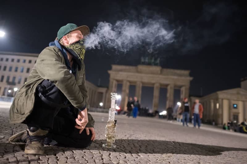 A man smokes a bong during a "Smoke In" in front of the Brandenburg Gate. From 01 April 2024, adults aged 18 and over will be allowed to possess 25 grams of cannabis in public places. In private areas, up to 50 grams of home-grown cannabis will be permitted. Sebastian Gollnow/dpa