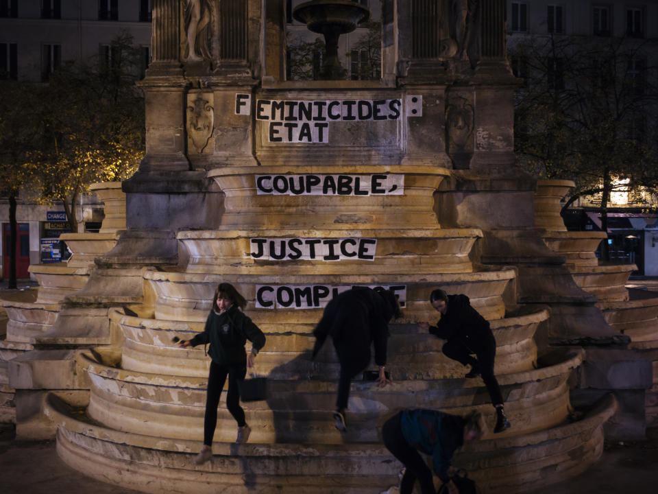 In this photo taken in the early hours of Monday Nov. 4, 2019, from left to right, Pauline, Clivia, France and Lea paste a slogan on a fountain reading " Femicides : guilty state, accomplice justice" in central Paris. About 300 women across France pasted slogans at the same time overnight from Sunday to Monday on courthouses in 27 different French cities to denounce the alleged inaction of the French government and demanding justice about femicides. (AP Photo/Kamil Zihnioglu)