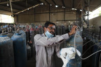 A worker refills medical oxygen cylinders at a charging station on the outskirts of Prayagraj, India, Friday, April 23, 2021. India put oxygen tankers on special express trains as major hospitals in New Delhi on Friday begged on social media for more supplies to save COVID-19 patients who are struggling to breathe. India's underfunded health system is tattering as the world's worst coronavirus surge wears out the nation, which set another global record in daily infections for a second straight day with 332,730. (AP Photo/Rajesh Kumar Singh)