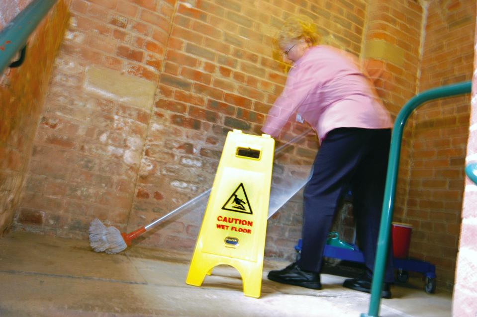 Cleaner mops the floor with health & safety warning sign in NHS building Yorkshire UK