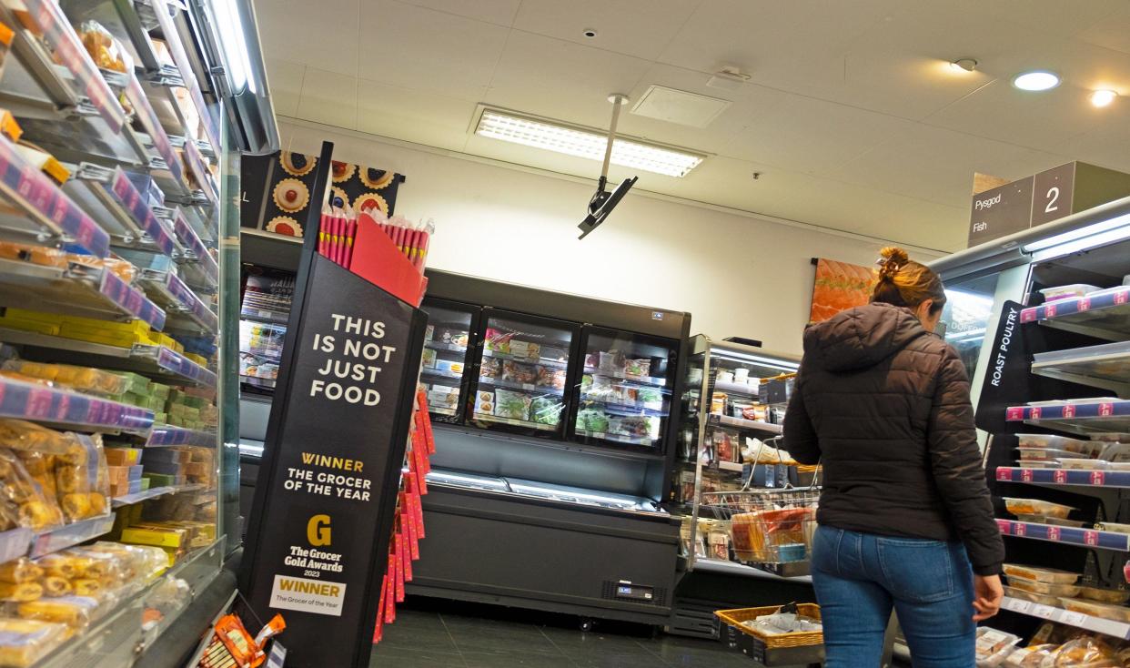 supermarket M&S store interior rear back woman looking at food on shelf The Grocer Gold Awards sign grocer of the year award in aisle inside store 2023 UK