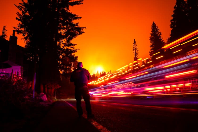 SHAVER LAKE, CA - SEPTEMBER 06: A vehicle streaks by in a long exposure as Fresno County Sheriff Deputy Jeffery Shipman stands along CA-168 as the Creek Fire creeps closer to town on Sunday, Sept. 6, 2020 in Shaver Lake, CA. (Kent Nishimura / Los Angeles Times)