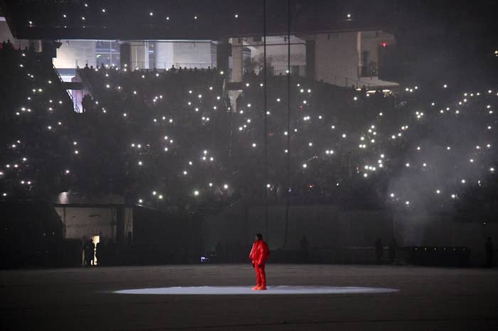 kanye west wearing all red standing in the middle of a stadium