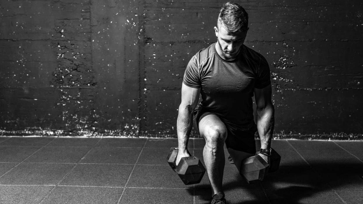  Dumbbell legs training, Young strong fit muscular sweaty man with big muscles strength cross workout training with dumbbells weights in the gym dark image with shadows real people black and white. 