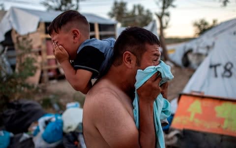 A man and a boy react to tear gas fired by Greek police in the camp following clashes - Credit: AFP