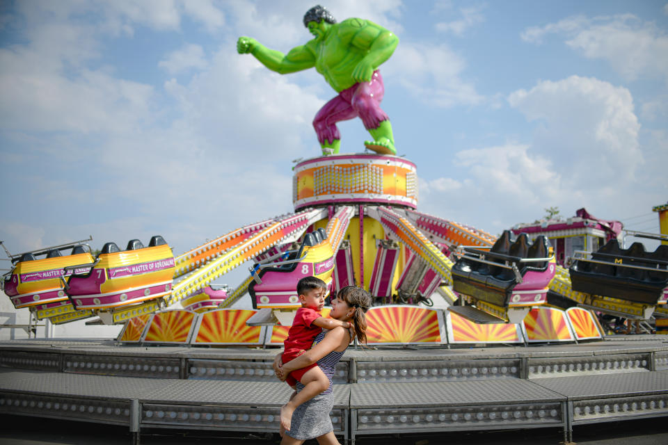 In this picture taken Saturday, Sept. 7, 2019, a girl carries a little boy by a merry go round at a fair in Calarasi, southern Romania. Romania's autumn fairs are a loud and colorful reminder that summer has come to an end and, for many families in poorer areas of the country, one of the few affordable public entertainment events of the year. (AP Photo/Andreea Alexandru)