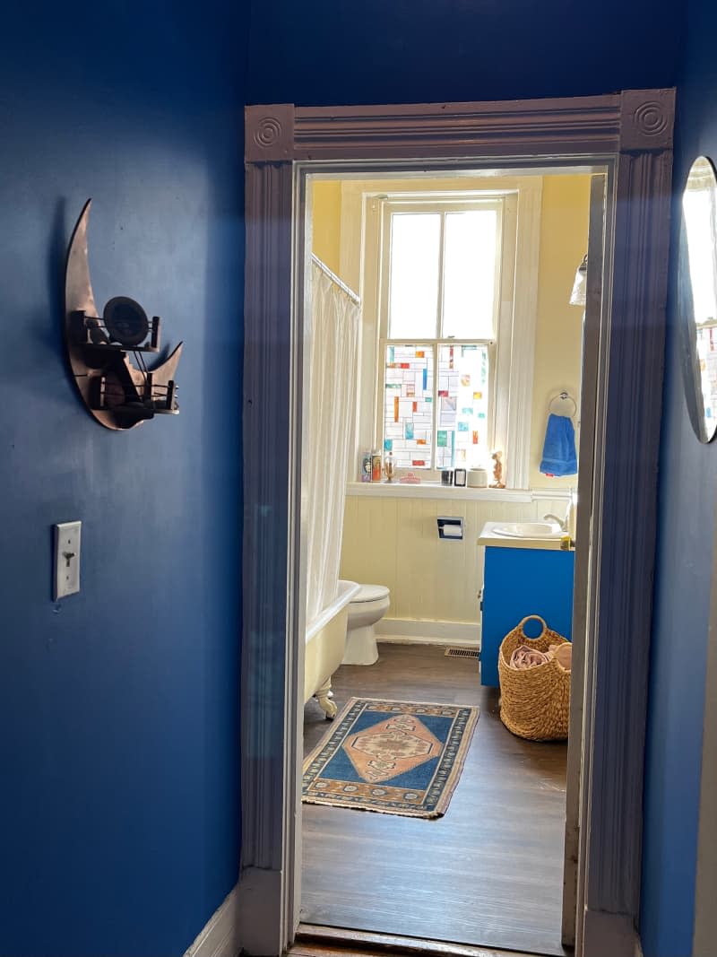 View of yellow bathroom with blue sink cabinet from blue hallway.