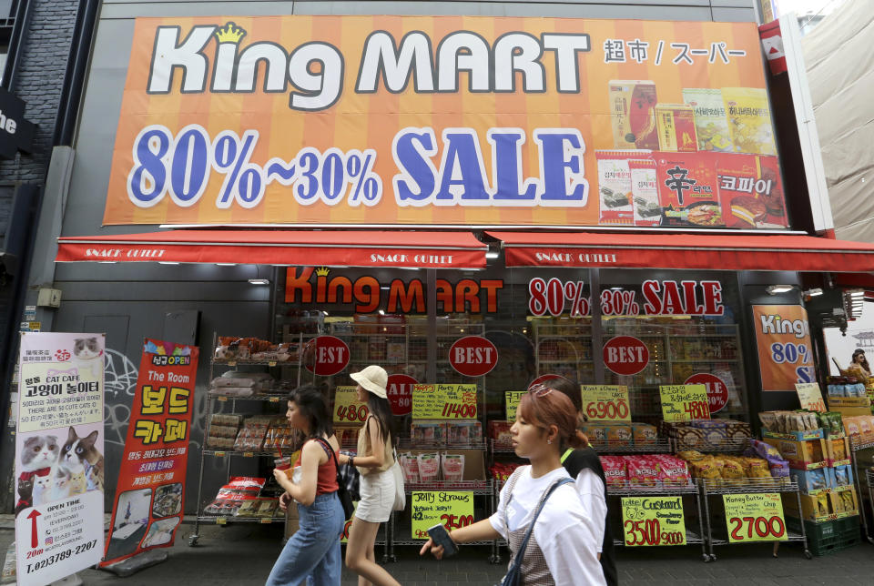 People pass by sale signs at a shopping district in Seoul, South Korea, Thursday, July 18, 2019. South Korea's central bank on Thursday cut its policy rate for the first time in three years to shore up growth threatened by a trade dispute with Japan. (AP Photo/Ahn Young-joon)