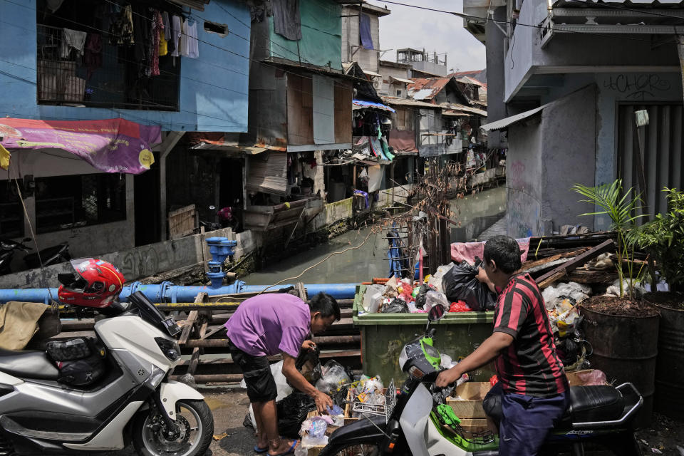 Men put garbage bags into an open dumpster in a low-income neighborhood in Jakarta, Indonesia, Tuesday, Jan. 25, 2022. Indonesian parliament last week passed the state capital bill into law, giving green light to President Joko Widodo to start a $34 billion construction project this year to move the country's capital from the traffic-clogged, polluted and rapidly sinking Jakarta on the main island of Java to jungle-clad Borneo island amid public skepticism. (AP Photo/Dita Alangkara)