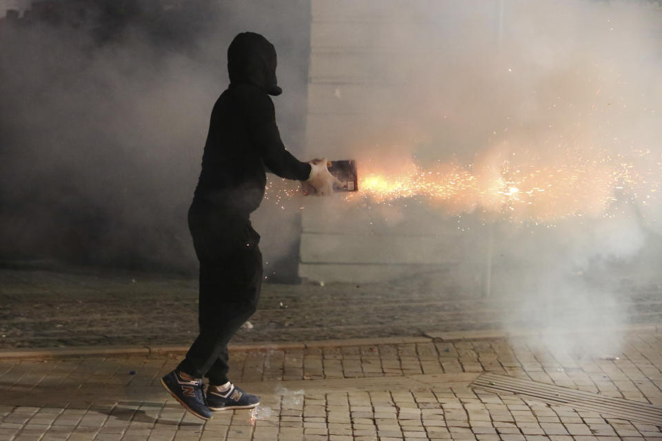 An hooded demonstrator shoots fireworks toward Albanian police officers during an anti-government protest in Tirana, Albania, Saturday, June 8, 2019. Thousands of Albanian opposition supporters are gathering in an anti-government protest while the United States and the European Union caution their leaders to disavow violence and sit in a dialogue to overcome the political crisis. (AP Photo/Hektor Pustina)