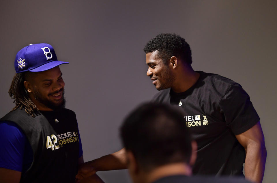 Cincinnati Reds' Yasiel Puig, right, is greeted by Los Angeles Dodgers relief pitcher Kenley Jansen as Puig speaks to reporters prior to a baseball game between the Dodgers and the Reds, Monday, April 15, 2019, in Los Angeles. (AP Photo/Mark J. Terrill)