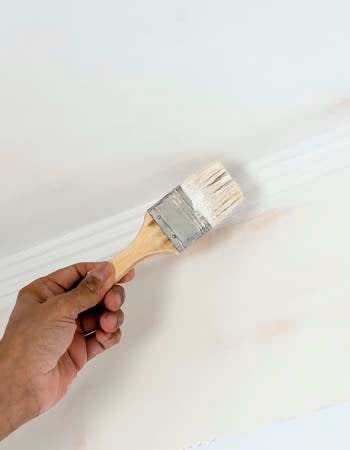 A close up of a person's hand using a paint brush to paint trim white. 