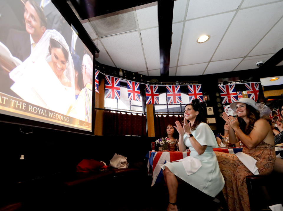 FILE - Lisa Casey, left, and Terry Campbell watch as the royal wedding of Britain's Prince Harry to Meghan Markle unfolds during a watch party at the Olde Ship British Pub & Restaurant, May 19, 2018, in Fullerton, Calif. The pomp, the glamour, the conflicts, the characters — when it comes to the United Kingdom’s royal family, the Americans can’t seem to get enough. (AP Photo/Chris Carlson, File)