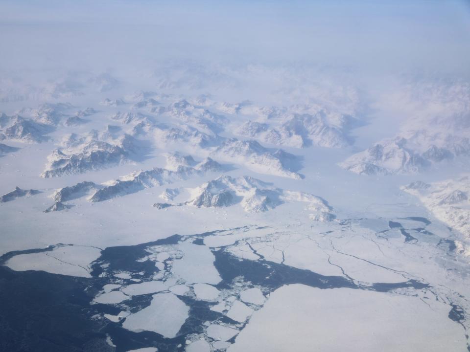 aerial view of snowy mountains ice fields above ice breaking up into the sea