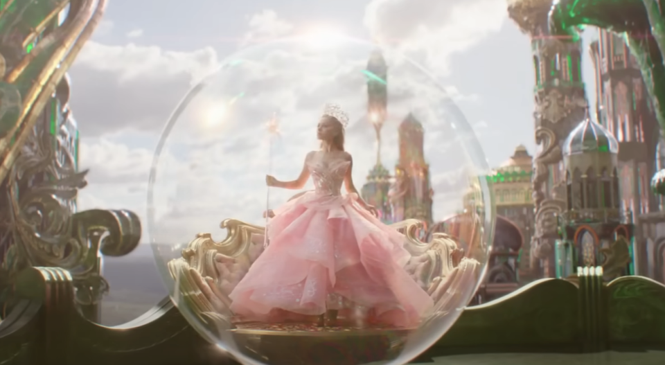 Ariana Grande in a sparkling gown inside a translucent bubble with a whimsical castle backdrop in "Wicked"