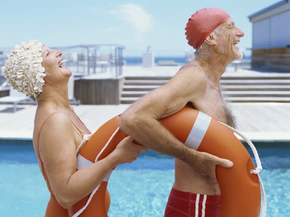 Two retirees in swimsuits holding a life preserver, laughing and smiling.