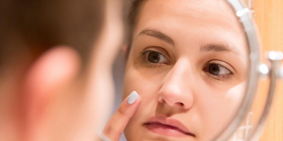 reflection of woman applying moisturizer on pimple in mirror at home