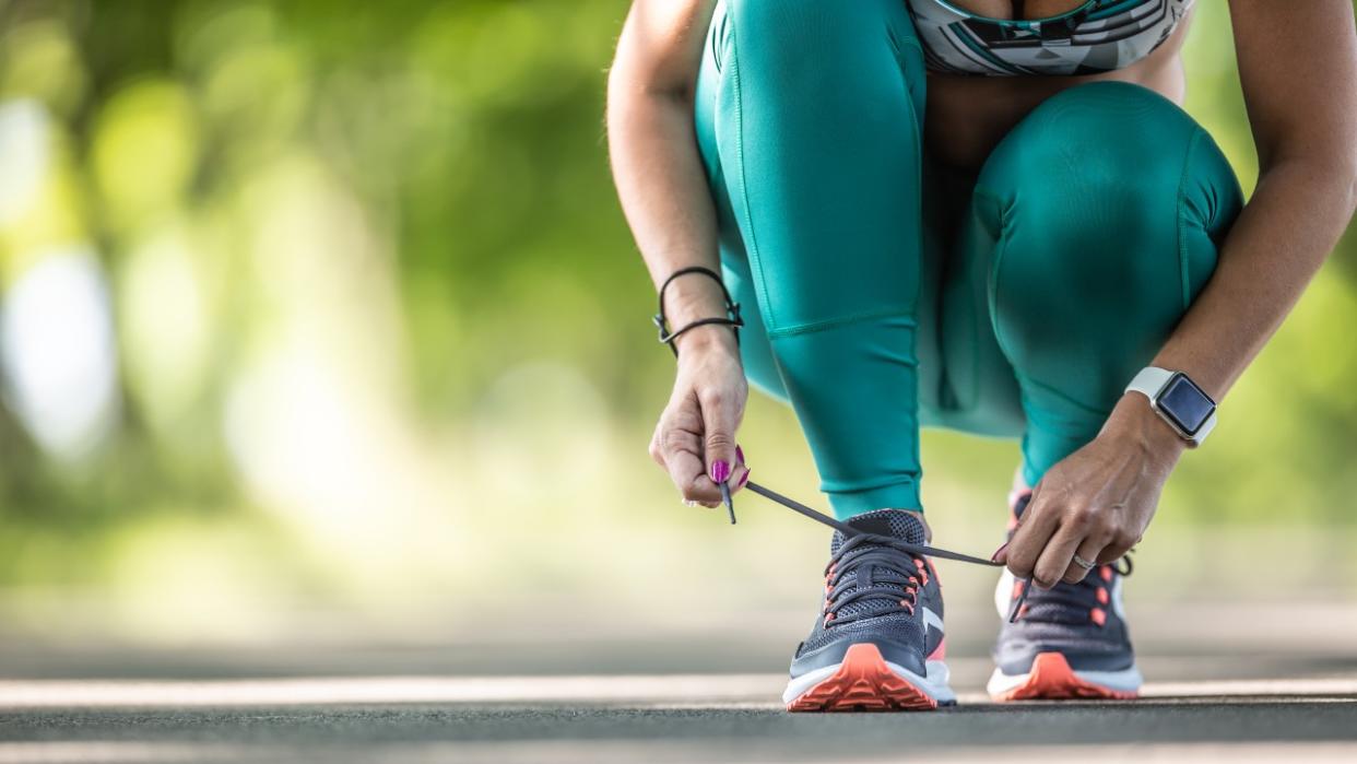  A crouching woman tying the laces of her running shoes, she is visible from the knees down 