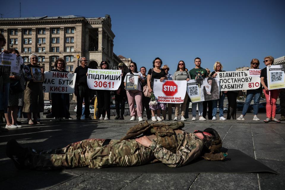 A protester performs the part of a dead soldier as relatives gather in memory of Ukrainian servicemen killed in the war (EPA)