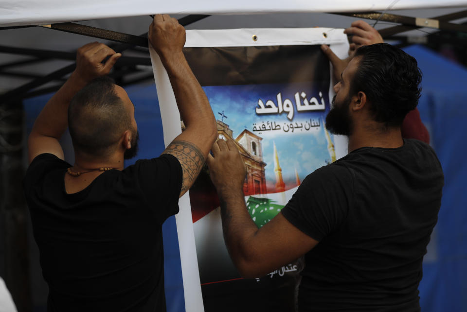 In this Thursday, Nov. 7, 2019, Shiite anti-government protesters install an Arabic placard that reads, " We are one, Lebanon without sectarianism," in downtown Beirut, Lebanon. Lebanon’s protests have brought out people from across the country’s spectrum of faiths and communities trying to throw out the entire ruling elite. They give a glimpse into a Lebanon transcending longtime divisions among Muslims, Christians and other sects. (AP Photo/Hussein Malla)