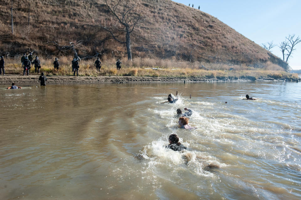 People swim across a river to where the police officers are standing guard.