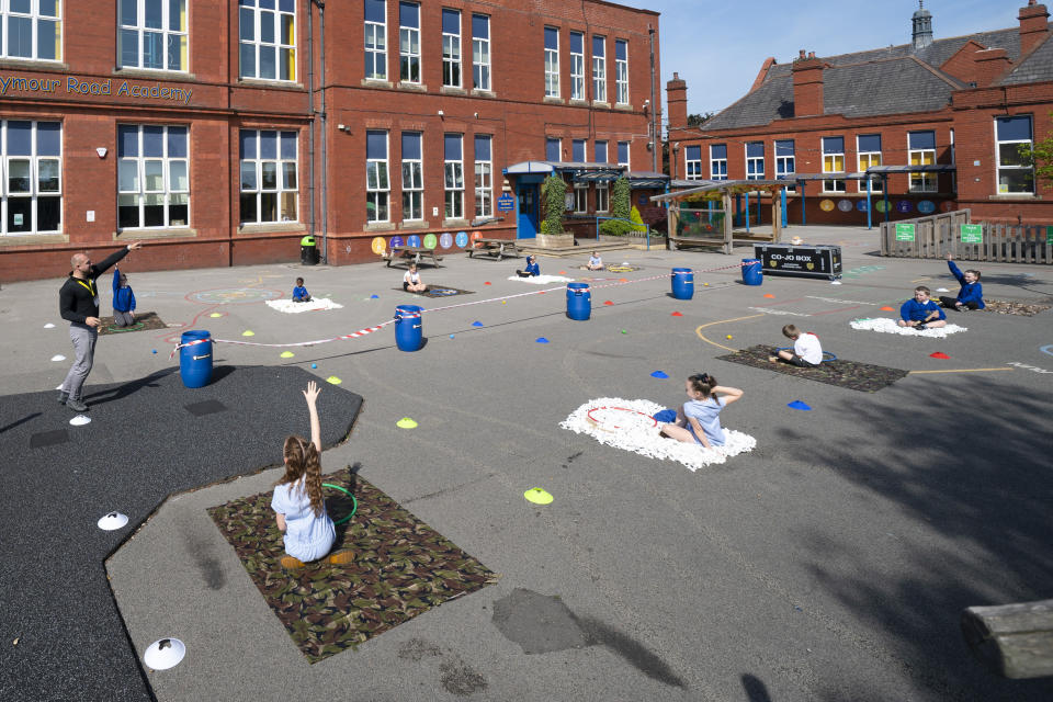 Former soldier Mike Hamilton, left, gestures as he interacts with children at Seymour Road Academy during a Commando Joe's character education program in Manchester, England, Wednesday May 20, 2020. Hula hoops, camouflage mats and tires aren't typical supplies needed during the coronavirus pandemic. But they're useful props as British veteran Mike Hamilton prepares to lead children in a military-style game designed to boost their resilience and mental health at a time of atypical stress. (AP Photo/Jon Super)