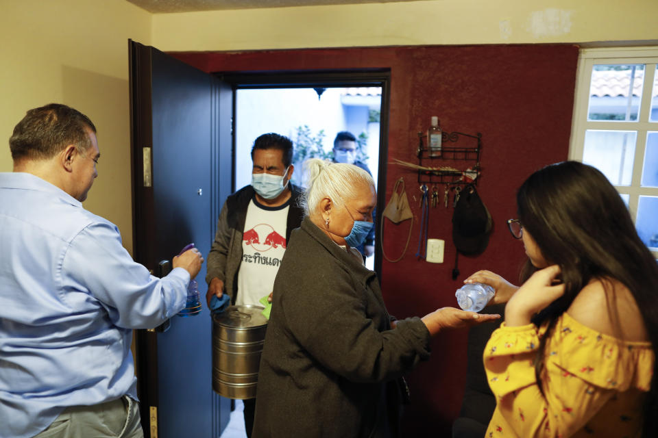 Ximena Canejo Hernandez, right, gives antibacterial gel to her grandmother Eloisa Santos Castillo, as Ximena's father, Alejandro Canejo Lopezk sprays disinfectant onto his in-laws, arriving for a simple event at home to mark Ximena's 15th birthday, in Tlalnepantla, just outside Mexico City, Monday, July 13, 2020. Ximena's family, wanting to give her a traditional quinceanera, had booked a church and event hall for July 18th long before the coronavirus pandemic hit, but the celebration had to be postponed until late November. The family had been following stay at home guidance, but with Mexico City's opening beginning in recent weeks, Ximena's grandmother decided to travel up from Oaxaca for her birthday, the first visit to her daughters and grandchildren in more than four months. (AP Photo/Rebecca Blackwell)