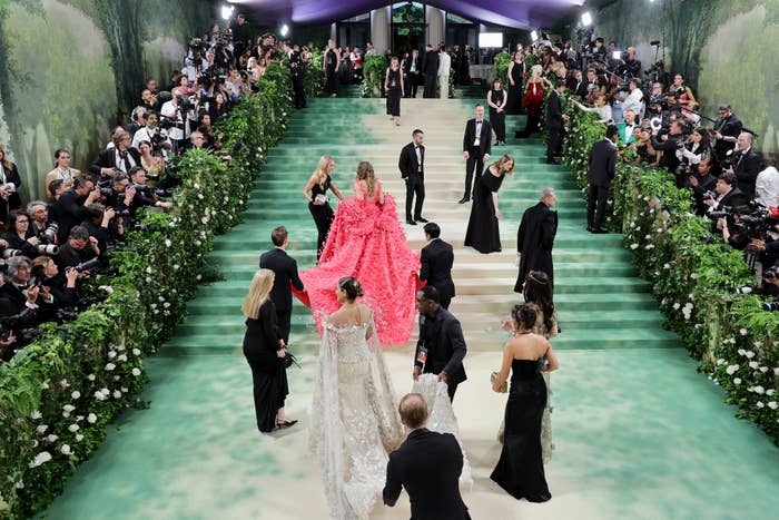 Elegant event with guests in formal attire; one individual stands out in a voluminous, ruffled gown ascending stairs