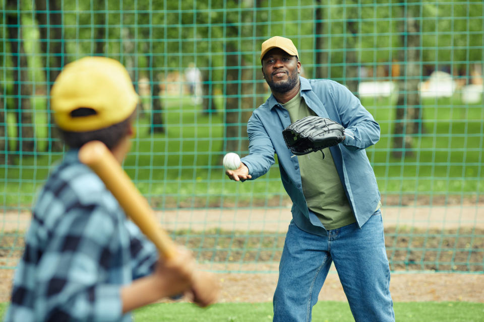 Um homem africano pega uma bola usando uma luva lançada por seu filho durante um jogo de beisebol ao ar livre