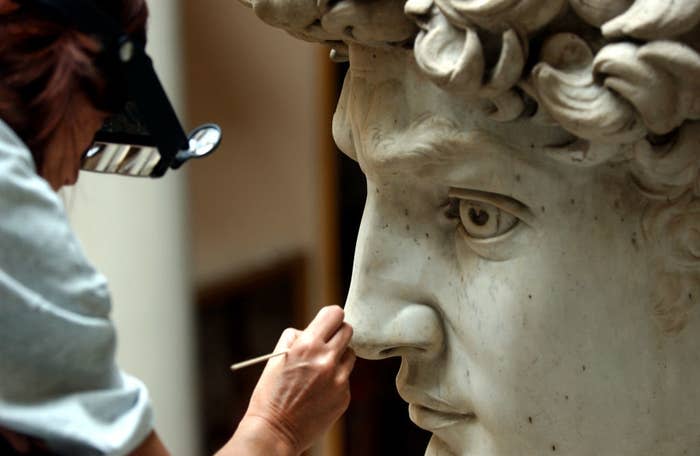 Close-up of a conservator restoring the face of Michelangelo's David, focusing on the nose while wearing magnifying glasses