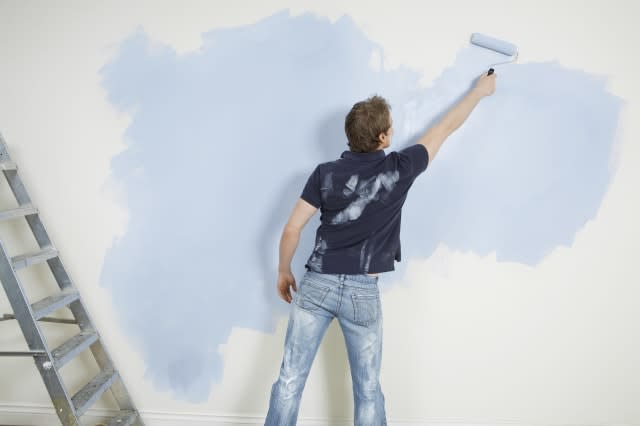 Rear view of young man painting wall with paintroller in unrenovated house
