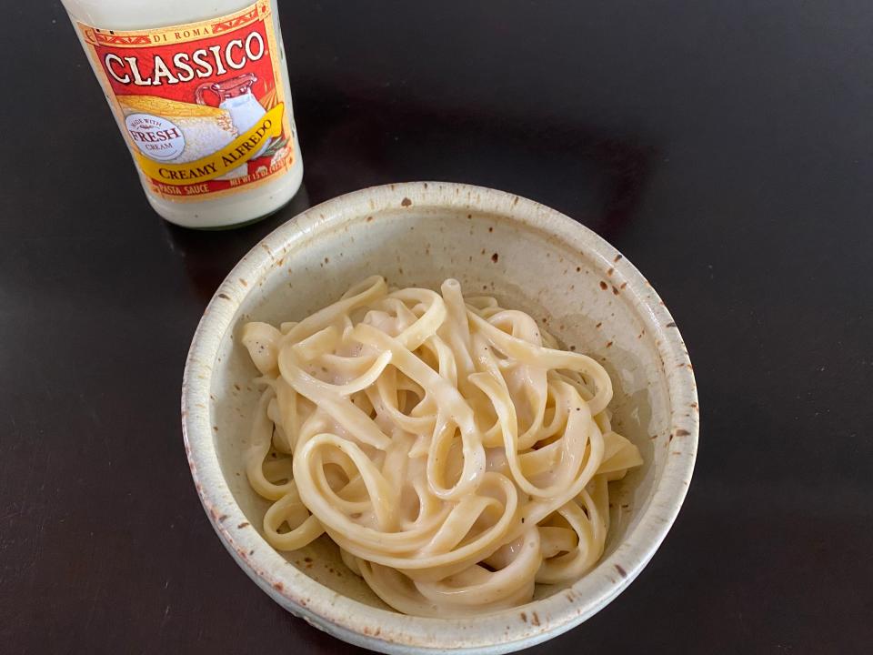 Alfredo sauce-covered noodles in a bowl with jar of Classico Alfredo next to it