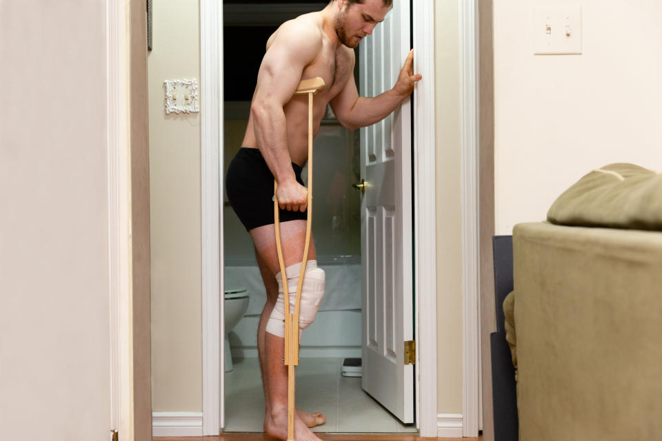 Man trying to step out of the bathroom on his crutches with his knee heavily bandaged after knee surgery