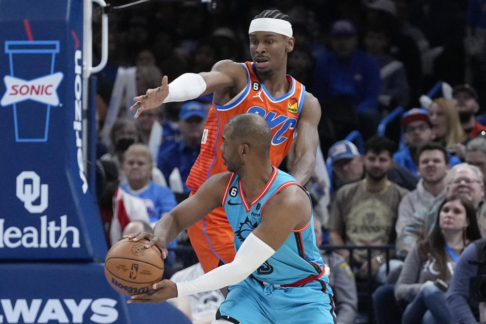 Phoenix Suns guard Chris Paul, front, passes around Oklahoma City Thunder guard Shai Gilgeous-Alexander, rear, in the first half of an NBA basketball game Sunday, March 19, 2023, in Oklahoma City. (AP Photo/Sue Ogrocki)